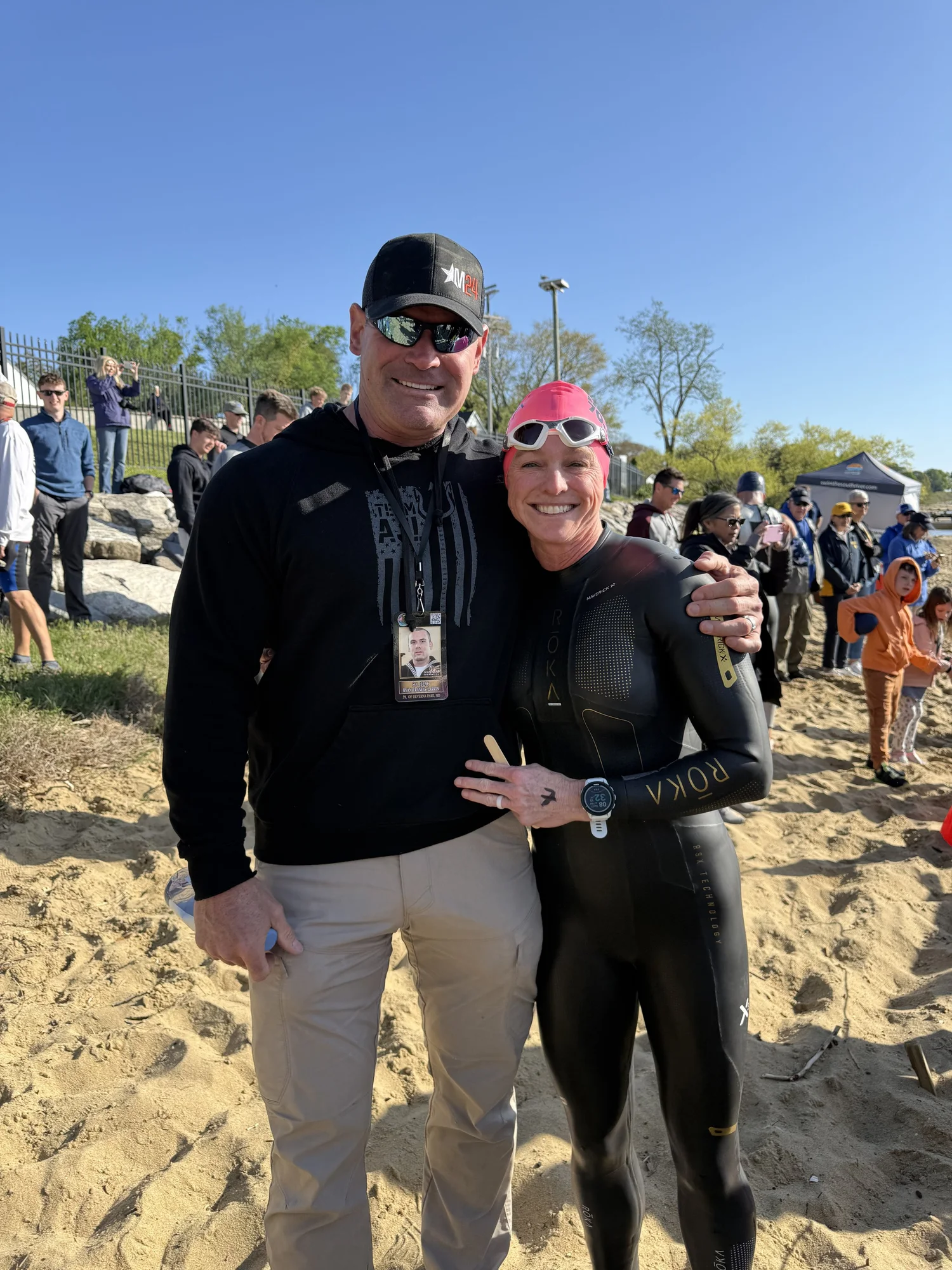 A man and woman in athletic gear smiling on a sandy beach before an endurance open water swim for the Navy SEAL Foundation.
